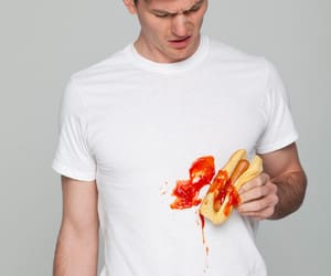 Young man wearing stained t-shirt holding hot-dog